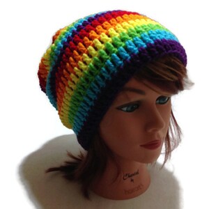 Puede incluir: Un gorro de punto de ganchillo arco&iacute;ris con un borde morado. El gorro est&aacute; en una cabeza de maniqu&iacute;.