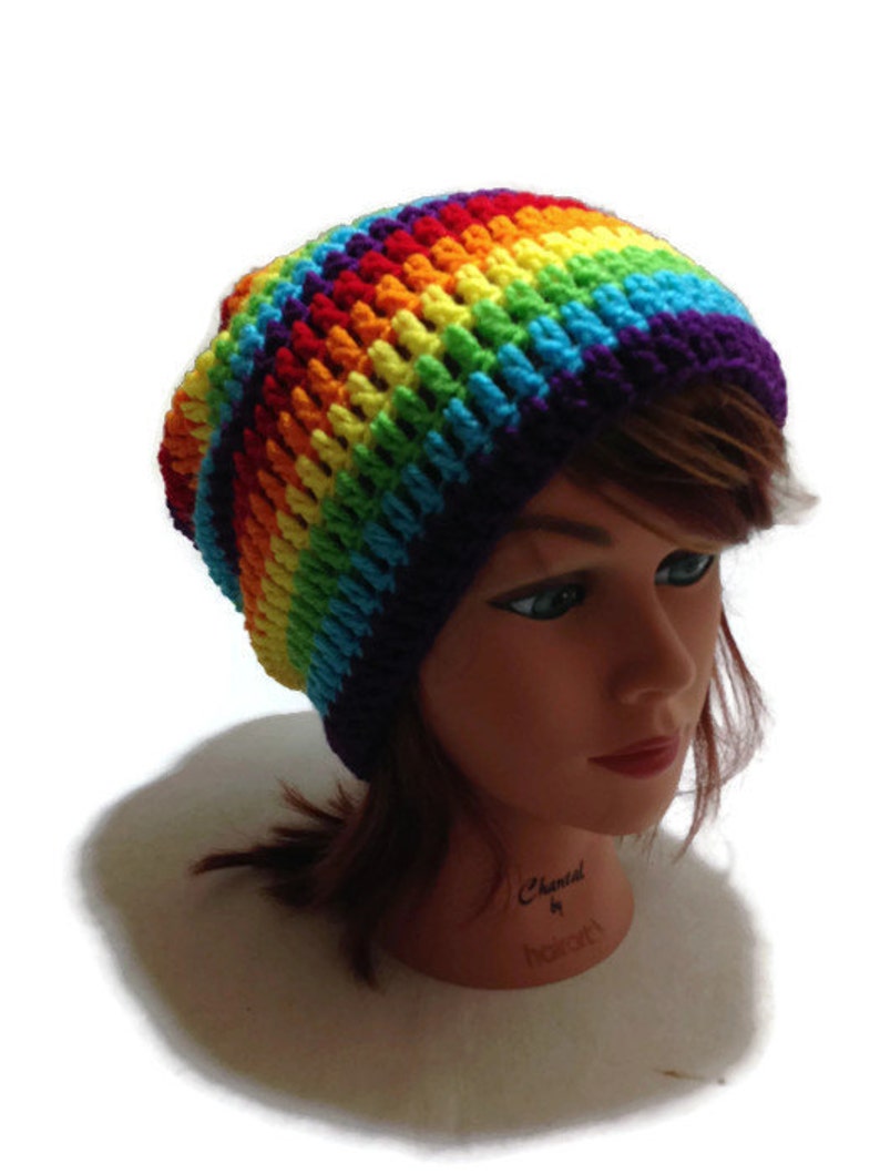 Puede incluir: Un gorro de punto de ganchillo arco&iacute;ris con un borde morado. El gorro est&aacute; en una cabeza de maniqu&iacute;.