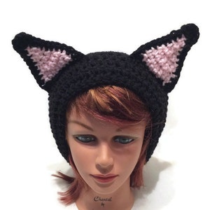 May include: Black crocheted cat hat with pink ears. The hat is on a mannequin head with red hair.