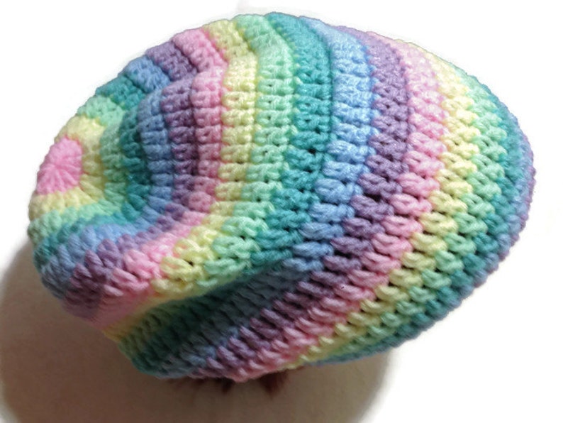 May include: A crocheted beanie hat in a rainbow color pattern of pink, yellow, green, blue, and purple.