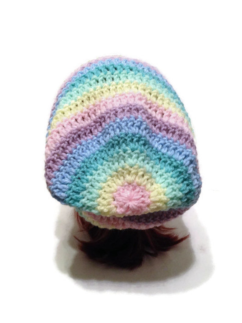 May include: A rainbow crochet beanie with a long ponytail coming out of the top. The beanie is made with pastel colors of pink, blue, green, and yellow.