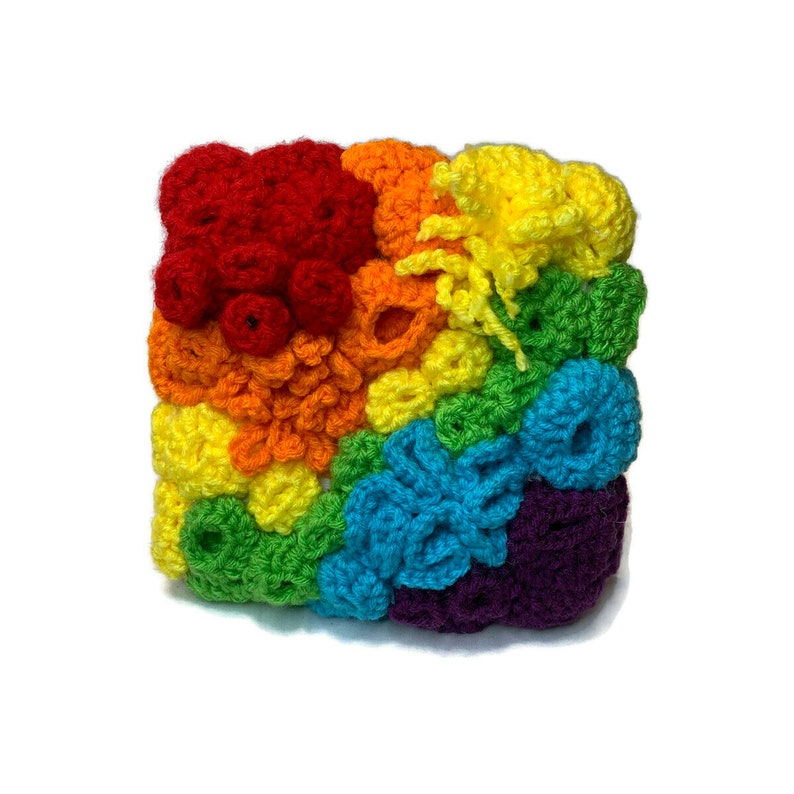 May include: A crocheted rainbow square with different textured stitches in each colour. The colours are red, orange, yellow, green, blue, purple.