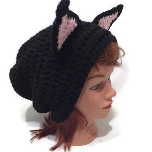 May include: Black crocheted beanie with pink cat ears. The beanie is slouchy and has a loose fit.