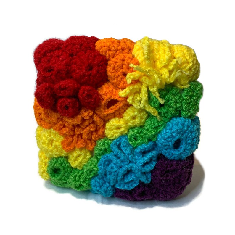 May include: A crocheted rainbow square with different textures and colours. The square is made of red, orange, yellow, green, blue, and purple yarn.
