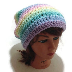 May include: A rainbow crochet beanie hat with a light purple, light blue, light green, yellow, and pink color pattern. The hat is on a mannequin head.