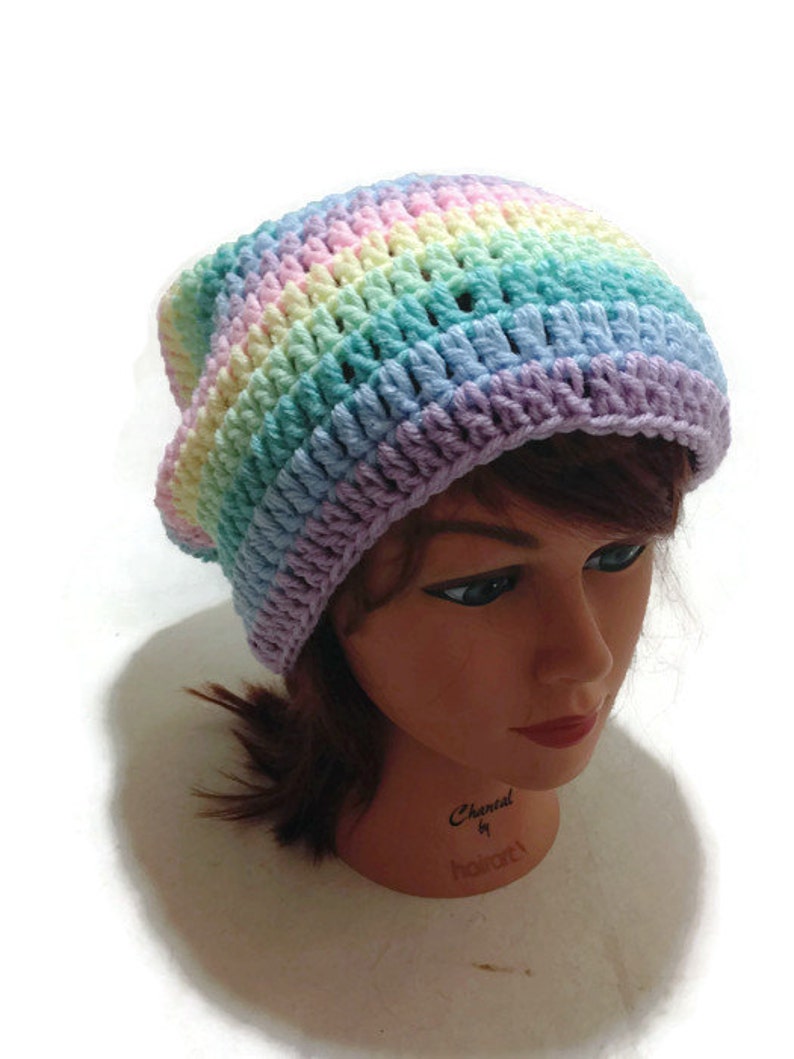 May include: A rainbow crochet beanie hat with a light purple, light blue, light green, yellow, and pink color pattern. The hat is on a mannequin head.