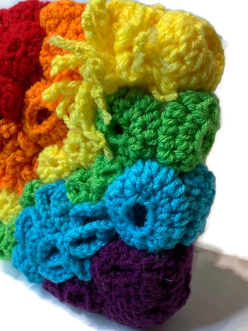 May include: A rainbow crocheted wall hanging with a textured, 3D design. The colours are red, orange, yellow, green, blue, purple, and a hint of white.