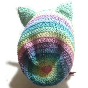 May include: A rainbow striped crocheted hat with cat ears. The hat is made with a variety of pastel colors, including pink, blue, green, and yellow.