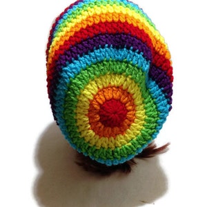 Puede incluir: Un gorro de punto de ganchillo arco&iacute;ris con un patr&oacute;n circular. El gorro est&aacute; hecho con hilo de colores en tonos de rojo, naranja, amarillo, verde, azul, a&ntilde;il y violeta.