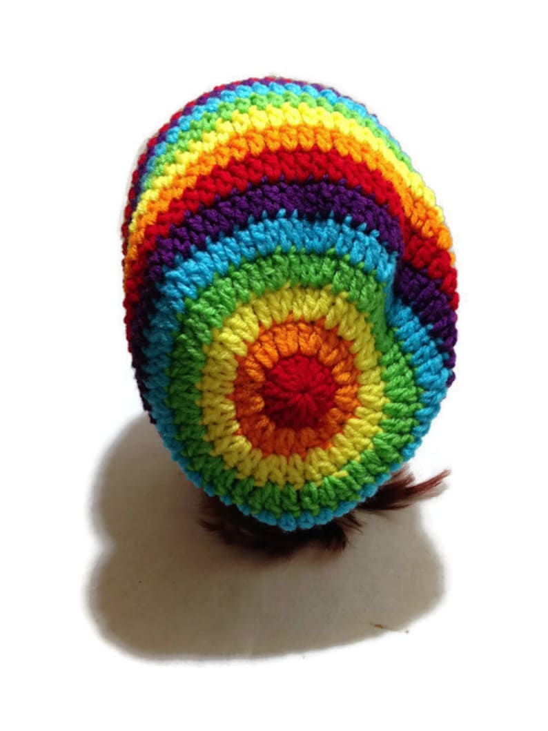 Puede incluir: Un gorro de punto de ganchillo arco&iacute;ris con un patr&oacute;n circular. El gorro est&aacute; hecho con hilo de colores en tonos de rojo, naranja, amarillo, verde, azul, a&ntilde;il y violeta.