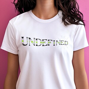 May include: White t-shirt with the word "UNDEFINED" in a black, green, and gray striped design. A sunburst graphic is to the right of the word. The shirt is short-sleeved.