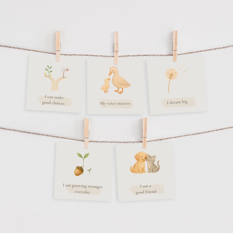 May include: Five square cards with inspirational messages are clipped to a string with wooden clothespins. The cards feature illustrations of a tree, ducklings, a dandelion, a sprout, and a puppy and kitten. Text includes phrases like "I can make good choices."