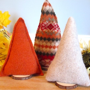 May include: Three cone-shaped ornaments made of knit fabric, each mounted on a small circular wooden base. One is solid orange, one features a multi-colored Fair Isle pattern in orange, red, and brown, and one is a solid light beige color.