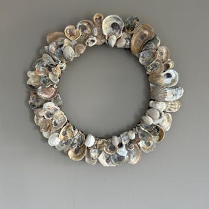 Peut inclure: Une couronne circulaire composée de divers coquillages aux tons de blanc, beige et marron. Les coquillages sont disposés de près, formant un anneau décoratif. La couronne est un élément de décoration intérieure sur le thème de la côte.