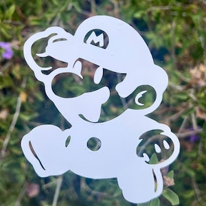 Peut inclure: Un autocollant en vinyle blanc représentant la silhouette stylisée du personnage Mario, dans une pose de course avec une casquette affichant la lettre M. Le motif est découpé dans une seule pièce de matériau, révélant les contours du personnage.