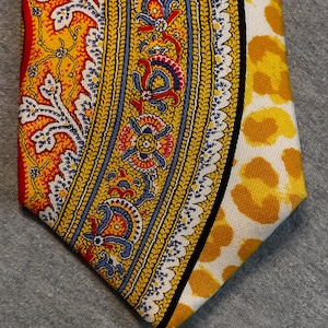 May include: A patterned necktie featuring a vibrant design. The tie showcases a combination of yellow, red, blue, and white colors. One side has a paisley-like pattern, while the other side has a yellow floral pattern on a white background.