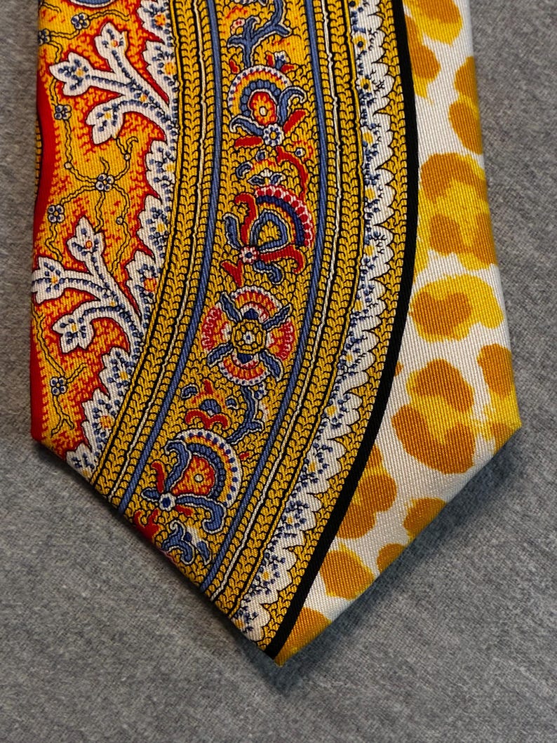 May include: A patterned necktie featuring a vibrant design. The tie showcases a combination of yellow, red, blue, and white colors. One side has a paisley-like pattern, while the other side has a yellow floral pattern on a white background.