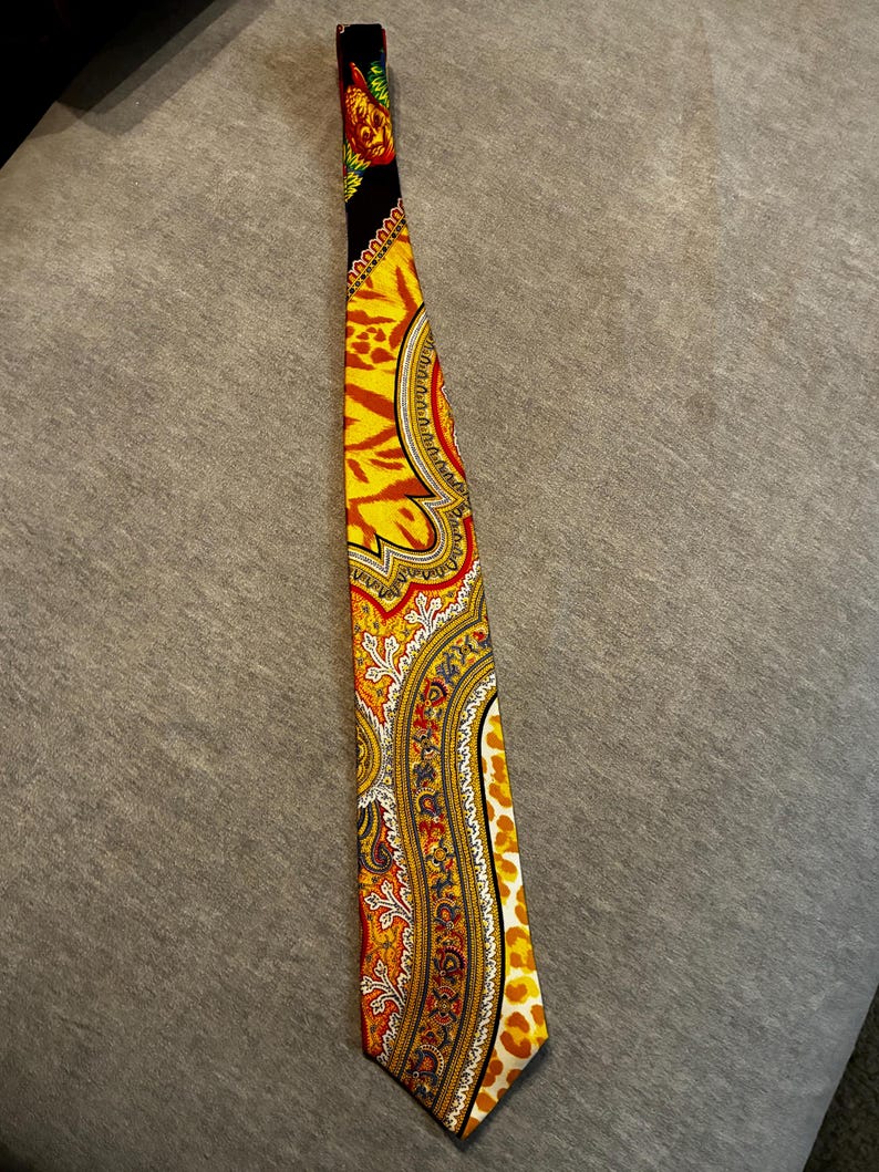 May include: A colorful necktie with a vibrant paisley pattern in shades of yellow, orange, and red. The tie features a black top section with a floral design and a leopard print on the edge. The tie is made of a silky material.