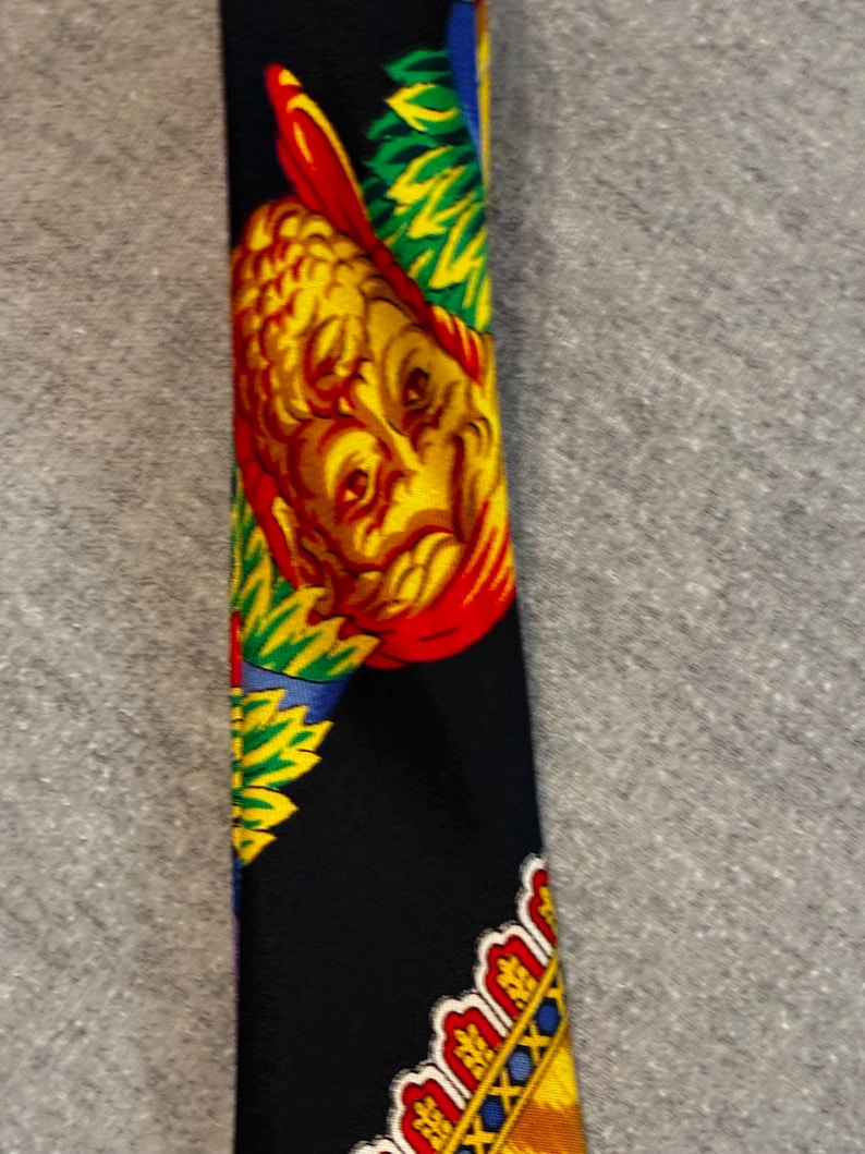 May include: A black necktie with a colorful pattern. The design features a yellow and red face, with green, blue, and yellow accents. The tie's bottom edge has a decorative border with red, yellow, and blue details.