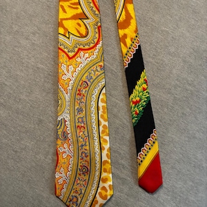 May include: A patterned necktie with a yellow, red, and white paisley design on one side and a black, red, and green design on the other. The tie has a vibrant color palette and a classic style.