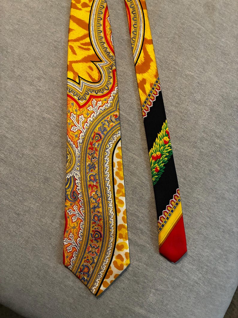 May include: A patterned necktie with a yellow, red, and white paisley design on one side and a black, red, and green design on the other. The tie has a vibrant color palette and a classic style.