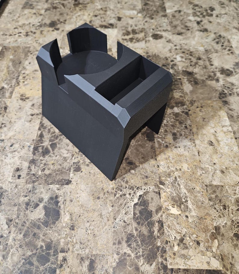 以下が含まれることがあります： 幾何学的なデザインの黒い3Dプリントデスクオーガナイザー。円形のホルダー、長方形のスロット、小さなコンパートメントがあります。オーガナイザーはマットブラックのプラスチック製で、モダンでミニマリストな美しさを持っています。