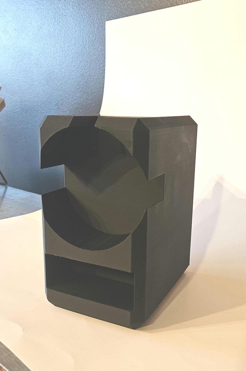 以下が含まれることがあります： 暗い灰色の幾何学的な彫刻で、立方体の基部があります。彫刻には、大きな円と長方形のスロットを含む、切り抜かれた形状があります。デザインはモダンで抽象的で、室内装飾に適しています。