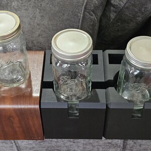 以下が含まれることがあります： 銀色の蓋が付いた、透明なガラス製のBallメイソンジャーが3つ。1つは湾曲した濃い色の木製スタンドに、他の2つは黒いホルダーに置かれています。ジャーは空で、すぐに使用できます。