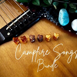 May include: Six small heart-shaped ear plugs in varying shades of amber, brown, and gold arranged in a row on a wooden guitar body. The text "Campfire Songs Bundle" is written in white cursive script across the center of the image.