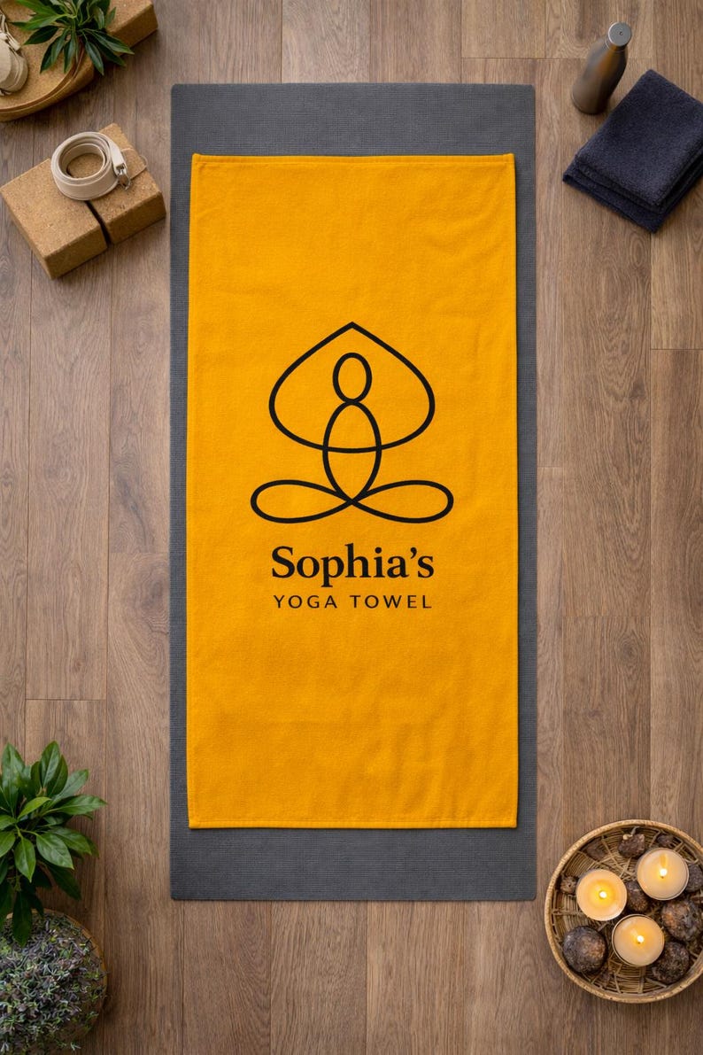 May include: A rectangular mustard yellow yoga towel featuring a black line art graphic of a person in a seated meditation pose. Below the graphic, the text reads Sophia's YOGA TOWEL in black, sans-serif and serif fonts, centered on the towel.