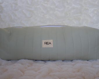 Può includere: Un beauty case rettangolare trapuntato verde chiaro con chiusura a cerniera. La borsa ha una piccola etichetta rettangolare con le lettere "REA". La borsa è appoggiata su una superficie bianca strutturata.