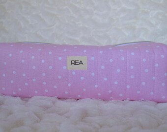 Può includere: Un astuccio rettangolare rosa a pois bianchi. L'astuccio ha una chiusura a cerniera e piccoli passanti in tessuto rosa su ciascuna estremità. Una piccola etichetta con le lettere "REA" è centrata sul davanti.