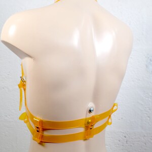 Product shot of a 2 story chest harness made from yellow transparent PVC with high quality steel buckles and rivets showing close up details of the item