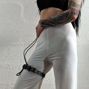 Leather thigh garter with one hanger and D-ring made from grey leather with high quality steel buckles and rivets worn by a woman in white trousers and black top