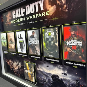 Peut inclure: Un cadre noir Call of Duty Modern Warfare Legacy Frame présentant sept inserts de pochettes de jeux individuels disposés en grille. L'affichage comprend des titres de la série avec des étiquettes numérotées et un fond sombre et atmosphérique.