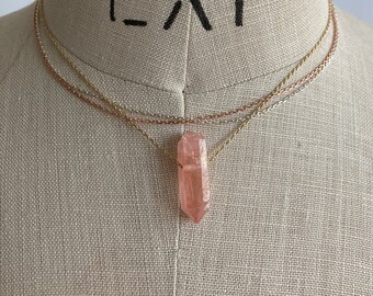 May include: A delicate layered necklace with a pink crystal pendant. The necklace features three chains in gold, silver, and rose gold.
