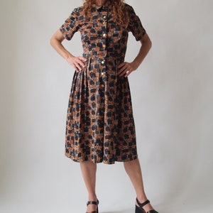 May include: A brown and black patterned midi dress with a collared neckline and short sleeves. The dress has a button-up front and a pleated skirt.