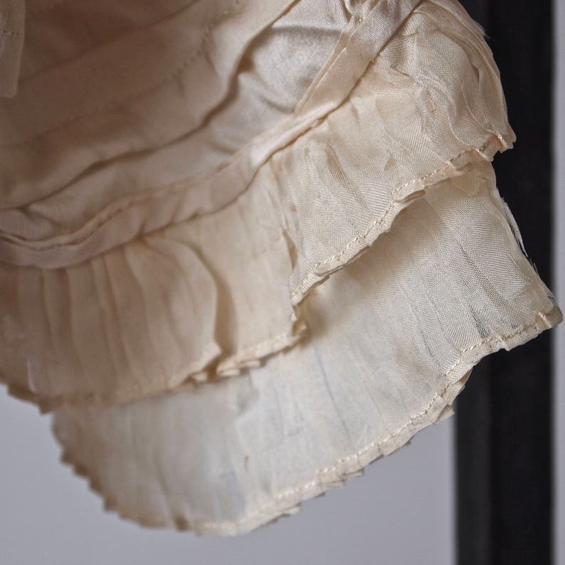 May include: Close-up of a white, ruffled fabric with a delicate, layered design. The fabric is soft and flowing, with a subtle sheen.