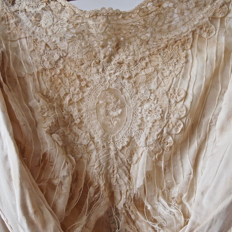 May include: Close-up of a delicate, cream-coloured lace fabric with intricate floral patterns. The lace is slightly frayed and worn, giving it a vintage aesthetic.