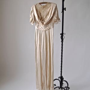 May include: A vintage ivory satin wedding dress with a lace bodice and short sleeves. The dress has a fitted bodice and a flowing skirt.