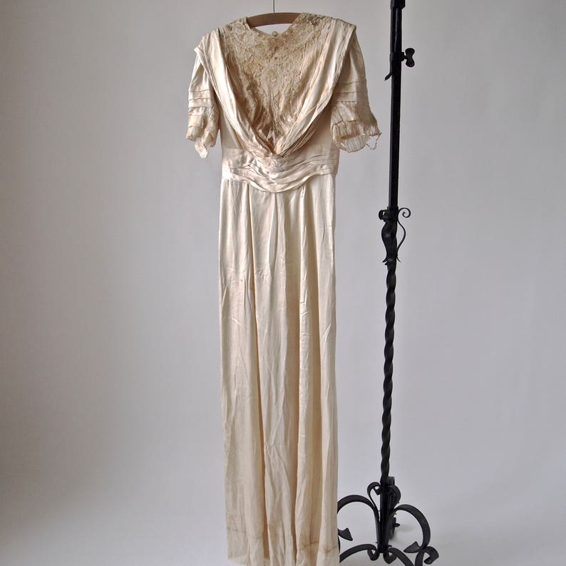 May include: A vintage ivory satin wedding dress with a lace bodice and short sleeves. The dress has a fitted bodice and a flowing skirt.