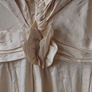 May include: A close-up of a white, ruffled fabric with a large, white fabric flower in the centre. The fabric is gathered and pleated, creating a textured look.