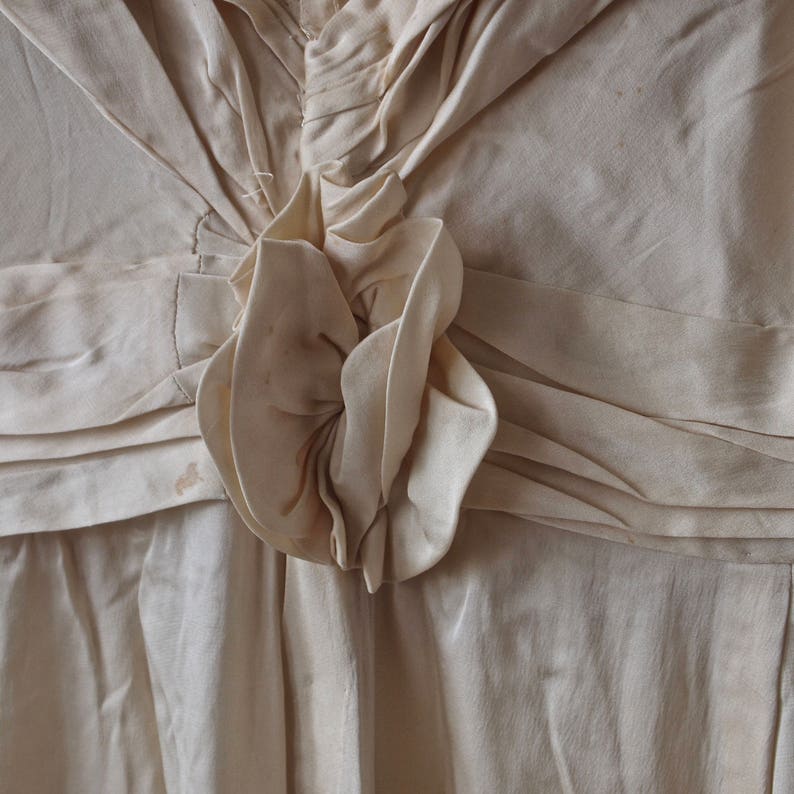 May include: A close-up of a white, ruffled fabric with a large, white fabric flower in the centre. The fabric is gathered and pleated, creating a textured look.