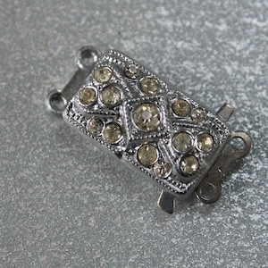 May include: Silver-toned clasp with a rectangular design featuring a geometric pattern of clear rhinestones.