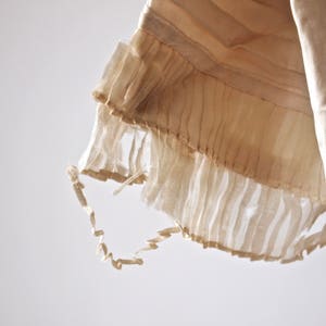 May include: A close-up of the bottom edge of a white garment with a delicate, ruffled trim. The trim is made of a sheer fabric and has a slightly frayed edge.