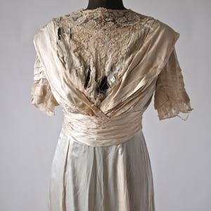 May include: A vintage ivory satin wedding dress with a lace bodice and a gathered skirt. The dress has a V-neckline and short sleeves. The lace is slightly damaged.