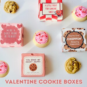 Könnte beinhalten: Eine Auswahl an Valentinstags-Keksschachteln und Keksen. Die Schachteln sind rosa und weiß mit Botschaften wie "A Little Treat For Someone Sweet" und "You Bake My Heart Happy". Zu den Keksen gehören glasierte Zuckerplätzchen und Schokoladen-Chip-Kekse.