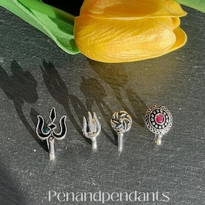 May include: A close-up shot features four silver nose studs with intricate designs, including a trident, a fork, a spiral, and a stud with a red gem. The studs are displayed on a dark surface, with the text "Penandpendant" visible.