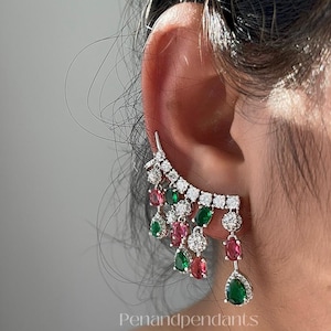 May include: Ear cuff earring with a cascade of gemstones. The earring features a curved design with clear, red, and green stones. The text "Penandpendants" is visible at the bottom.