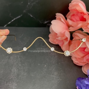 May include: A gold-toned metal hair accessory featuring a wavy, curved design adorned with clear, sparkling rhinestones arranged in floral and circular patterns. The text Penandpendants is printed in small white letters along the center wire.